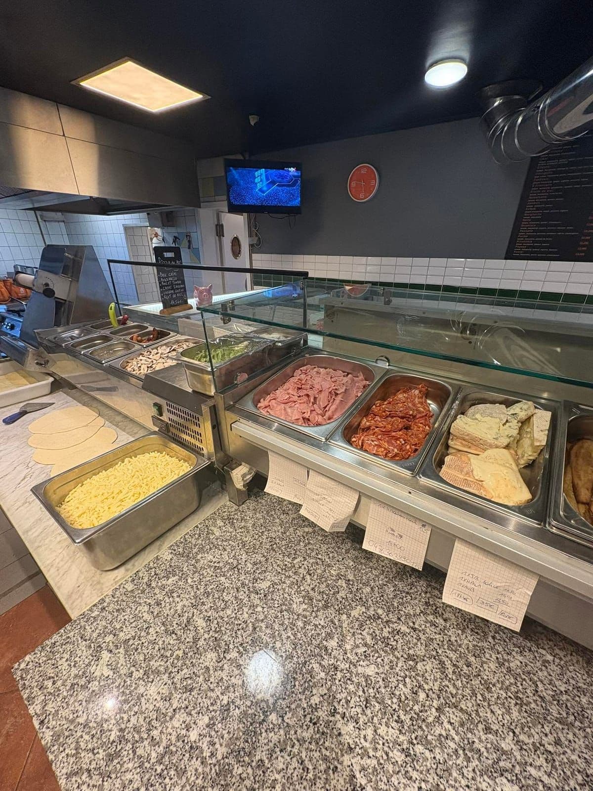 Le comptoir de la pizzeria : la vitrine réfrigérée des garnitures, le plan de travail en granit et la cuisine derrière