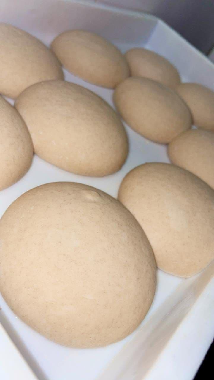 Des pâtons de pâte à pizza posés côte à côte dans un bac, avant d'être étalés
