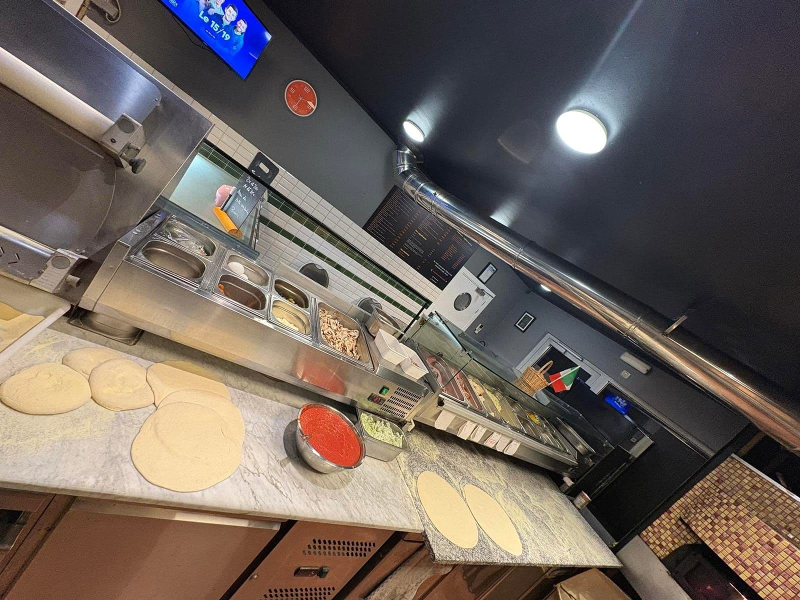 Le plan de travail pendant le service : des pâtons étalés, un bol de sauce tomate et les bacs de garnitures